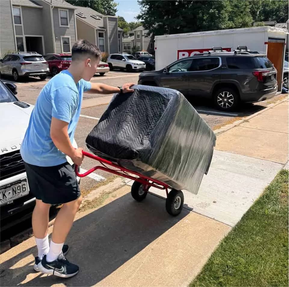 Mover pushing a wrapped sofa on a dolly to the truck