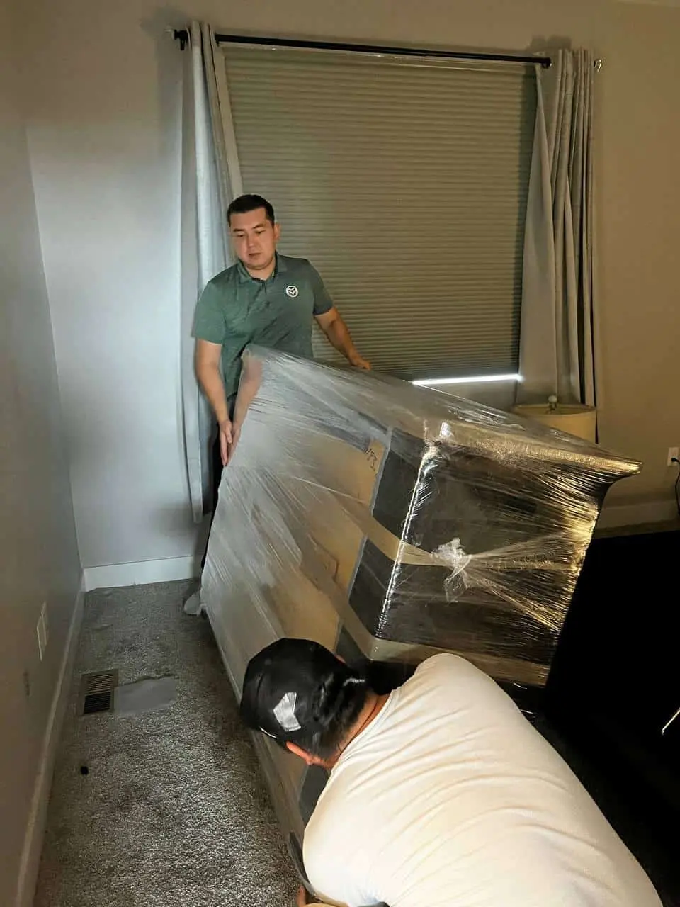 Two movers tilting a wrapped item through a doorway